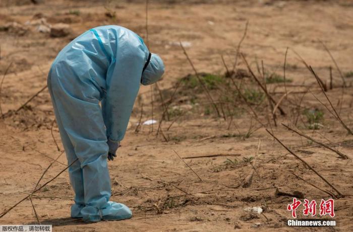资料图:印度新德里的墓地里,在埋葬死于新冠病毒的中央后备警察部队(CRPF)工作人员前,一名医护人员弯下了腰。
